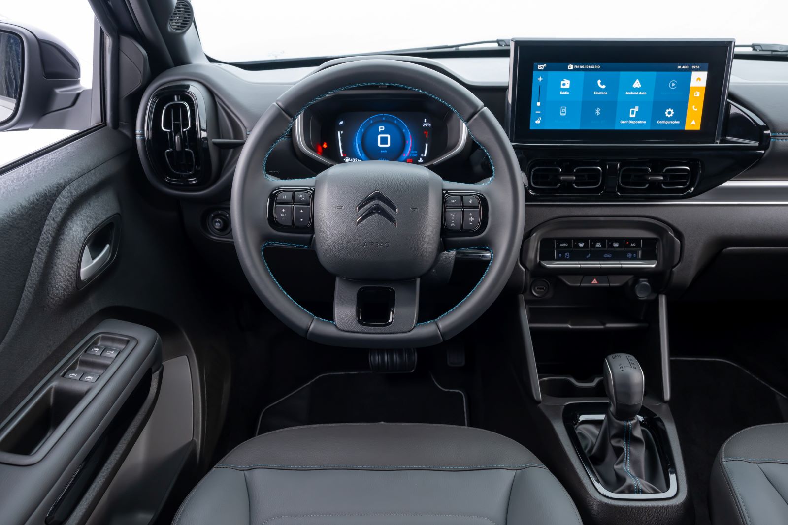 Painel de controle interno de um carro, com volante e tela multifuncional visíveis.